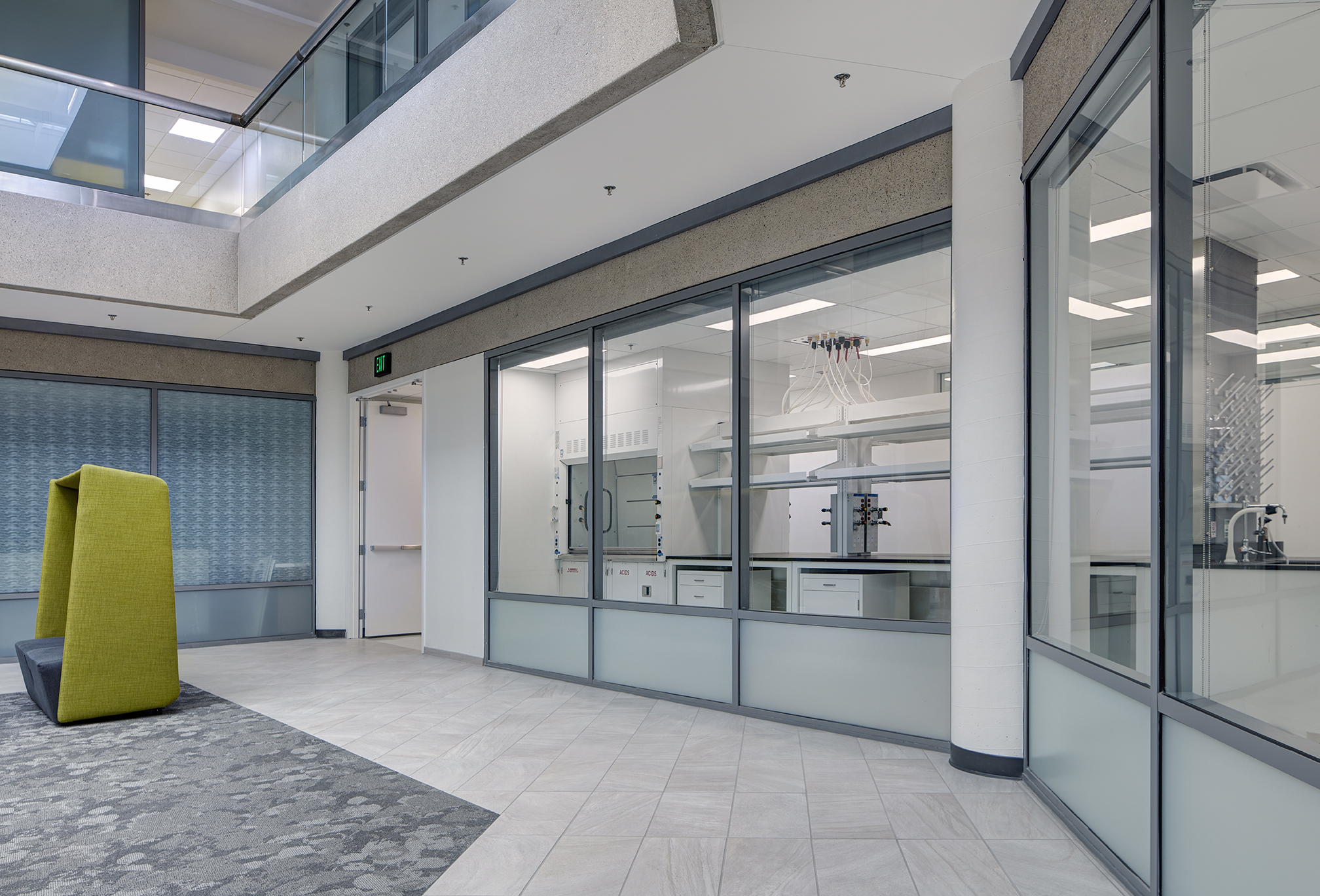 Looking through a large glass wall, at an angle at a lab. A chartreuse privacy chair is outside the window.