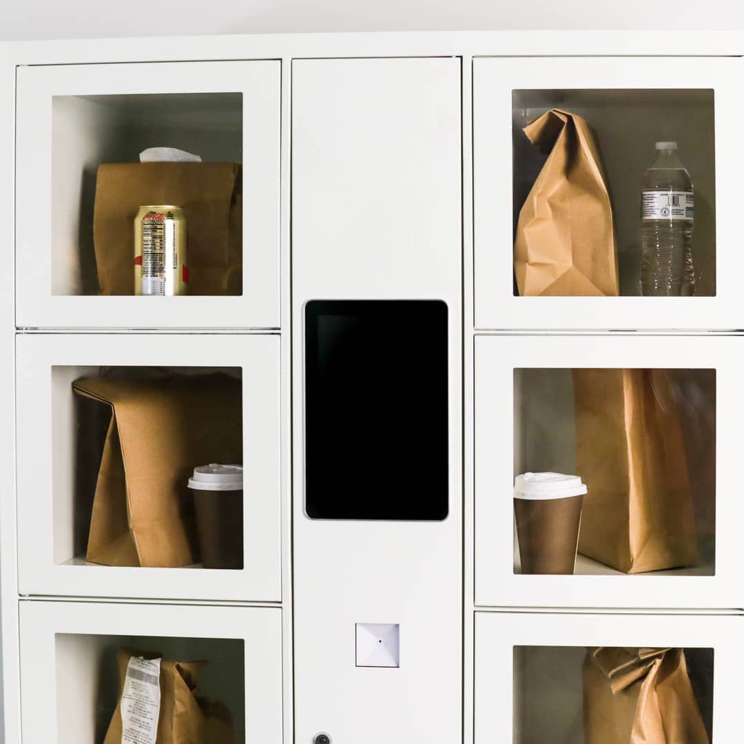 refrigerated locker with glass fronts each holding a brown bag lunch