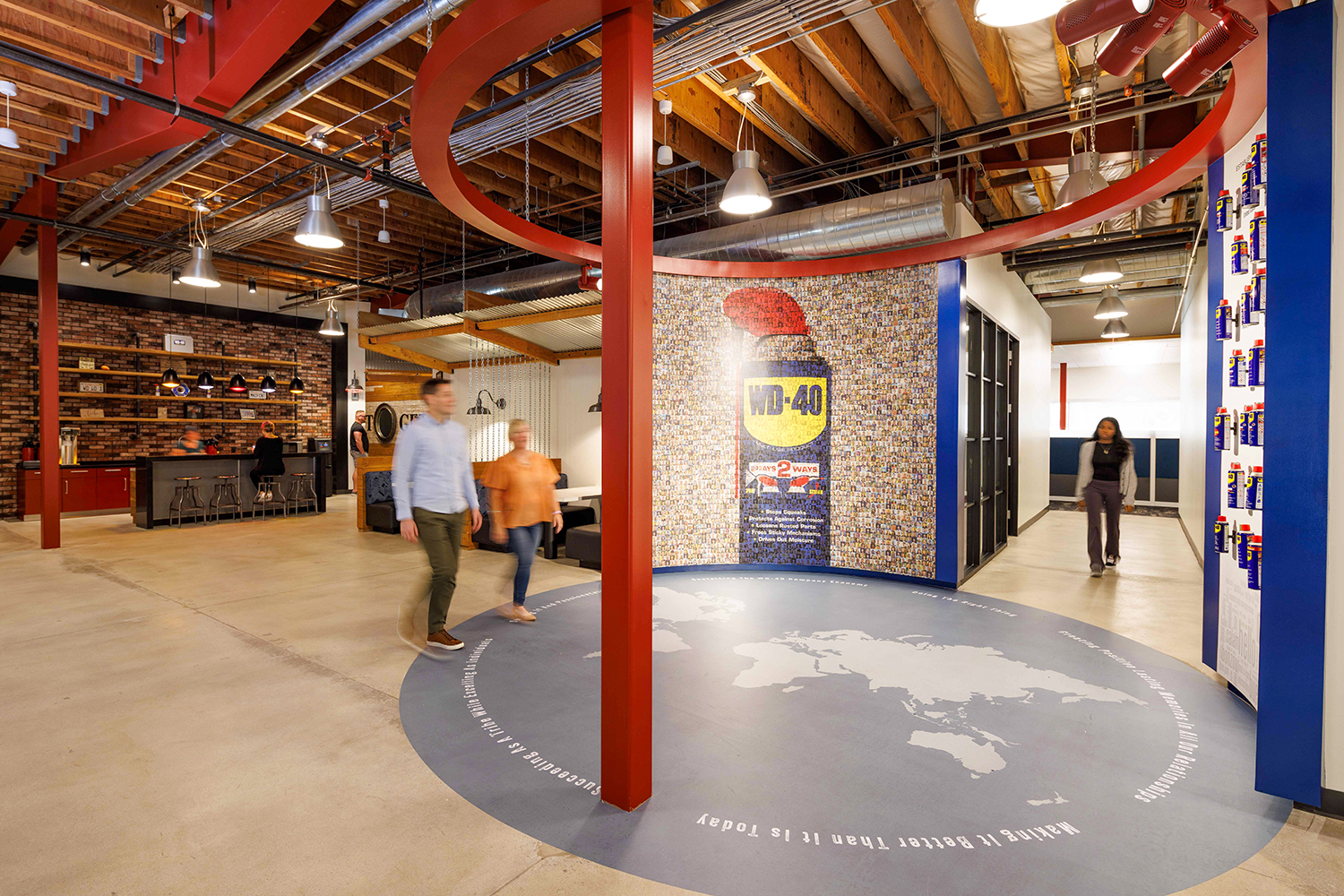 Near an area with a coffee bar, several people are walking towards a wall of WD-40 Company's new Culture Experience, including a display of cans of WD-40 from around the world and a graphic of a can of WD-40 made from thousands of small pictures of WD-40 employees.