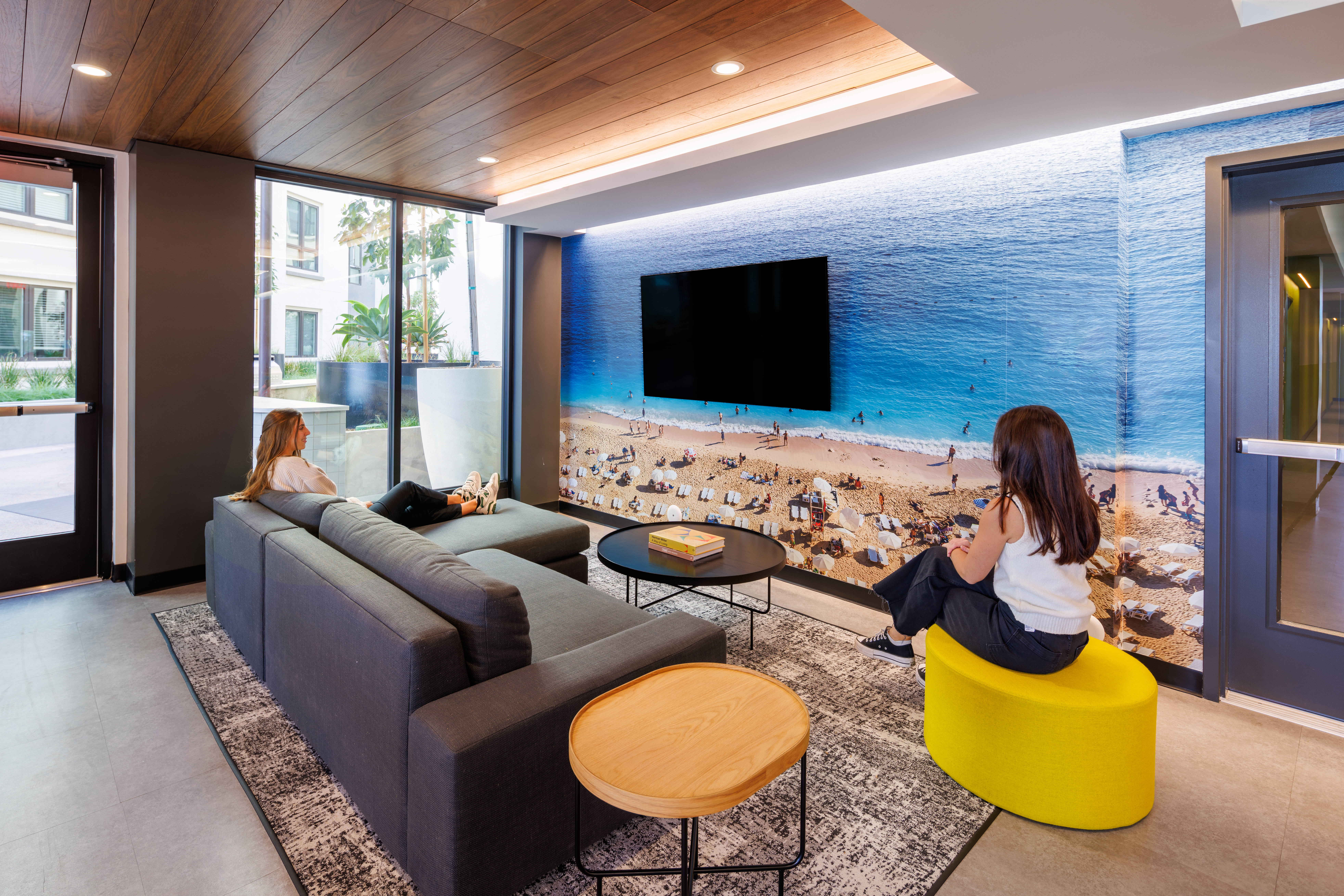 Coastal-inspired student housing interior with driftwood tones, surfboard accents, and ocean-inspired mural and sand-colored tiles in San Diego